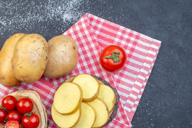Bovenaanzicht van hele en gehakte rauwe aardappelen op houten plank tomaten aan de rechterkant op zwart wit mix kleuren achtergrond