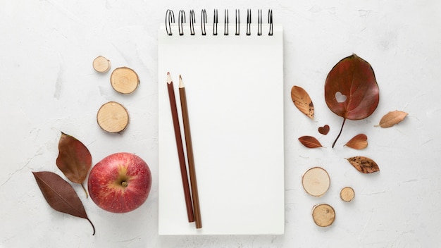 Foto bovenaanzicht van herfstbladeren met notebook en appel