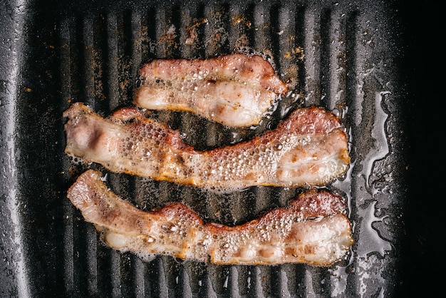 Bovenaanzicht van het bakken van sissende spekreepjes in een pan met hete smerende spekolie voor het maken van knapperig spek. met kopie ruimte. Keto-snackmaaltijd.