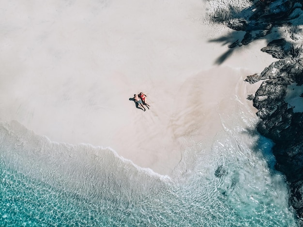 Bovenaanzicht van het gelukkige paar zonnebaden op het witte strand, turquoise water; huwelijksreis concept.