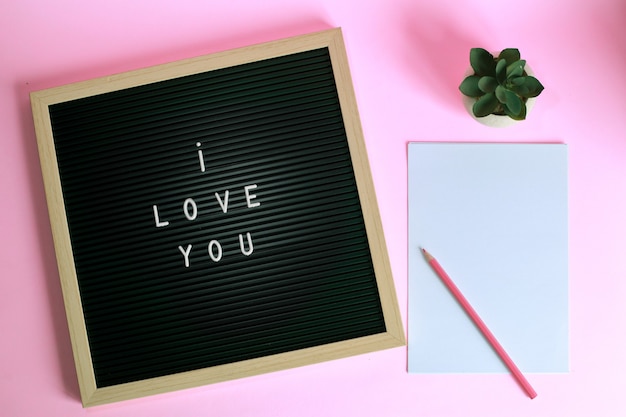 Bovenaanzicht van I LOVE YOU op letterbord met sappig en potlood op blanco papier geïsoleerd op roze achtergrond