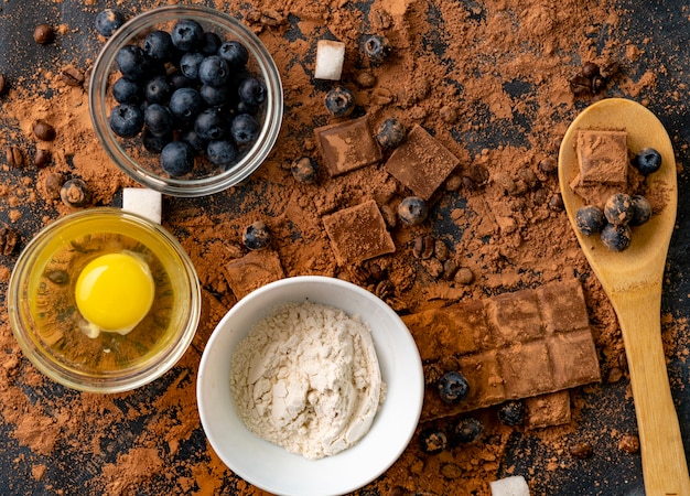 Bovenaanzicht van ingrediënten voor het koken of bakken van chocolade op tafel, bosbes, ei, bloem, cacao en chocolaatjes