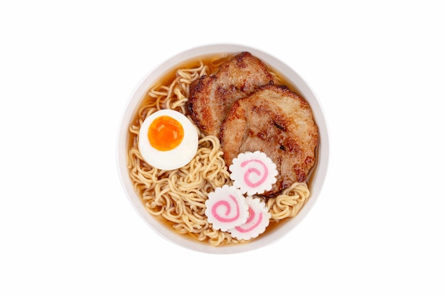 Bovenaanzicht van Japanse noedelsoep ramen in witte keramische kom met noedels, vleesbouillon, gesneden geroosterd varkensvlees, narutomaki, ei met dooier op pastelbeige achtergrond. Traditioneel gerecht van Japan, close-up