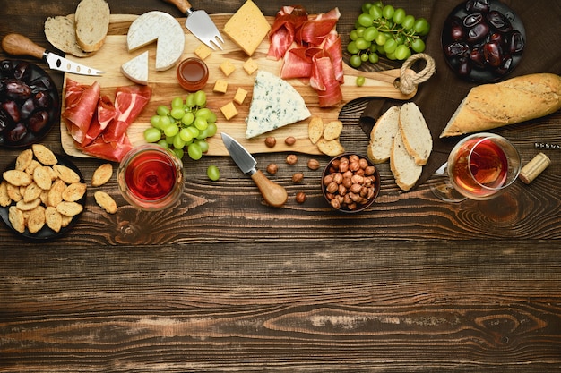 Bovenaanzicht van kaasplateau met prosciutto, druiven, honing, dadels, crackers, noten en wijn