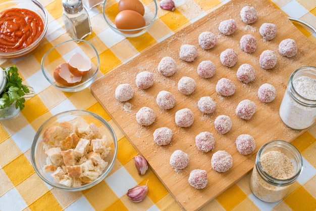 Bovenaanzicht van keukentafel met gehaktballen klaar voor pan, houten snijplank en rauwe ingrediënten