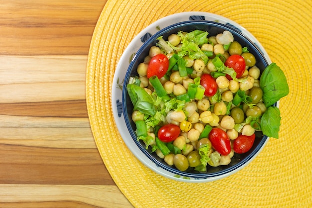 Bovenaanzicht van kikkererwten met bladeren, olijven en tomaten in een blauwe kom op tafel