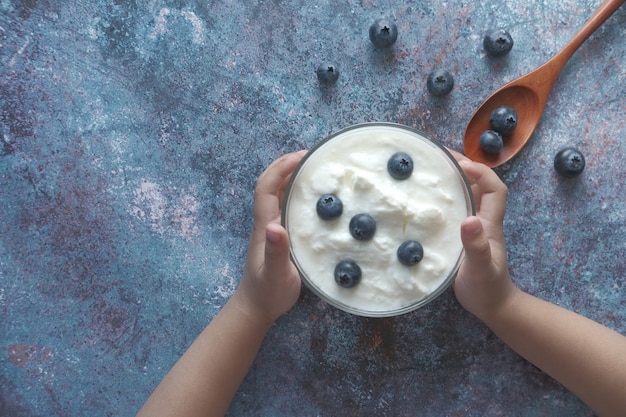 Bovenaanzicht van kind hand met een kom verse yoghurt met blauwe bes