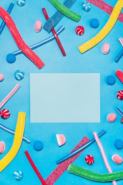 Bovenaanzicht van kleurrijke suikersuikergoed en lollies met envelop in het midden geïsoleerd op blauwe achtergrond
