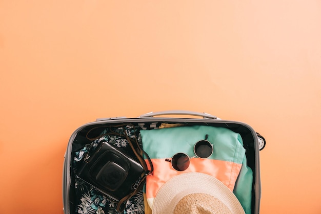 Bovenaanzicht van koffer met zomeraccessoires en filmcamera op oranje achtergrond