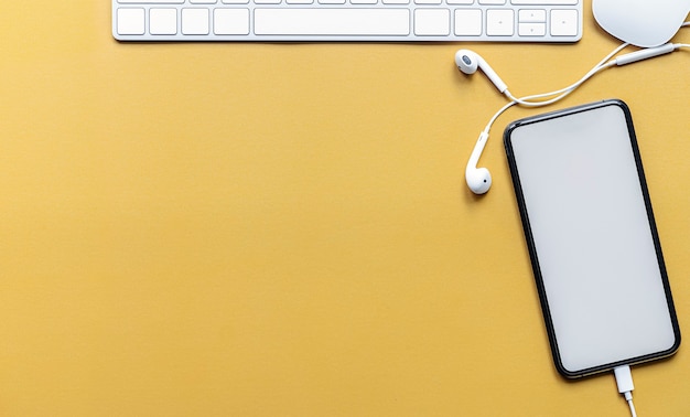 Bovenaanzicht van leeg scherm smartphone met witte computertoetsenbord en muis op gele achtergrond.