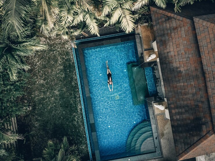 Bovenaanzicht van luxehotel: palmen, groen gazon, pannendak en het blauwe zwembad met een mooi meisje dat daar zwemt; recreatie concept.