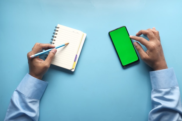 Bovenaanzicht van man hand met behulp van slimme telefoon en schrijven op Kladblok