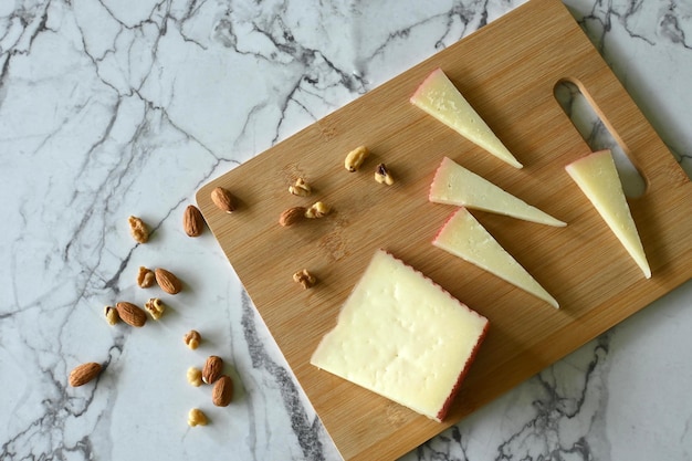 Bovenaanzicht van Manchego-kaas op snijplank, op marmeren tafel met kopieerruimte