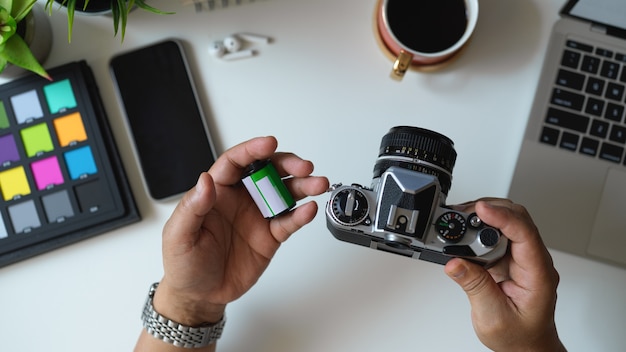 Bovenaanzicht van mannelijke fotograaf camera en camerafilm op zijn hand in de werkruimte