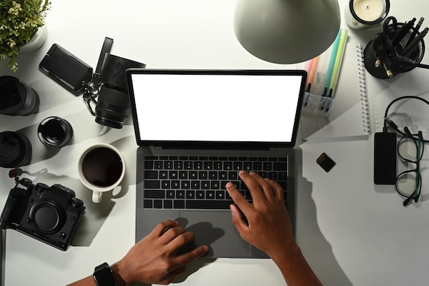 Bovenaanzicht van mannelijke fotograaf met behulp van laptop op witte tafel met digitale camera geheugenkaart en lens