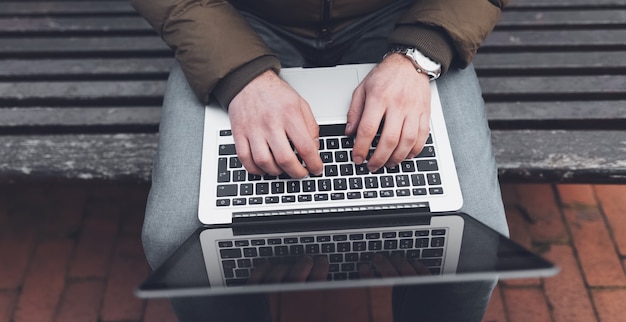 Bovenaanzicht van mannelijke handen typen op toetsenbord van laptop buitenshuis.