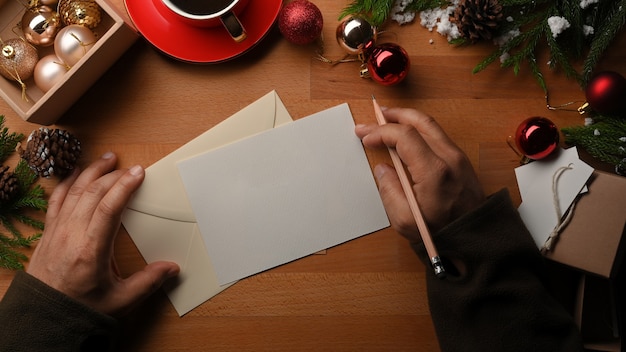 Bovenaanzicht van mannelijke handen wenskaart schrijven op houten tafel versierd met kerstversiering