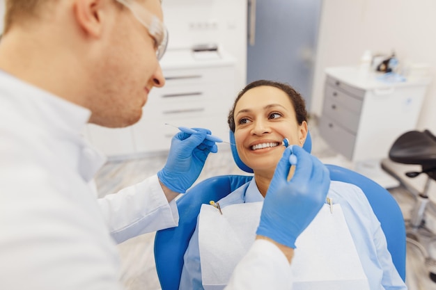 Bovenaanzicht van mannelijke tandarts die de tanden van de vrouwelijke cliënt controleert met spiegel in moderne privékliniek