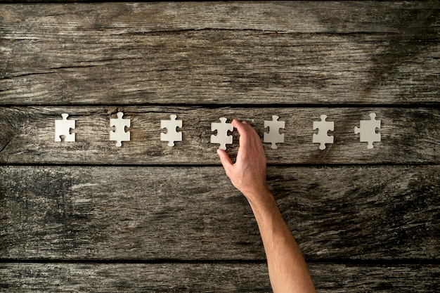 Bovenaanzicht van mannenhand zeven lege puzzelstukjes op een rij plaatsen