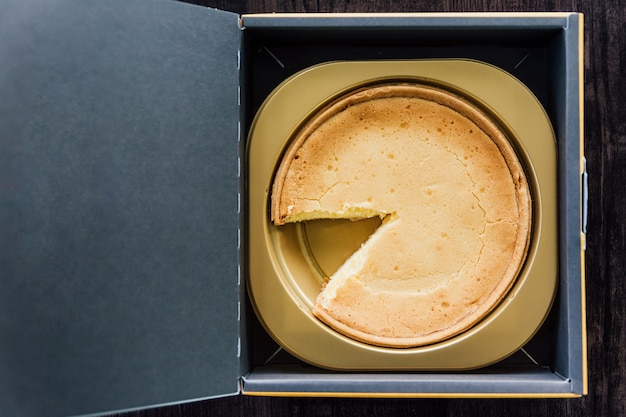 Bovenaanzicht van mascarpone crème brulee cheesecake met ontbrekende plak, zachte, rijke melkachtige smaak in papieren doos.