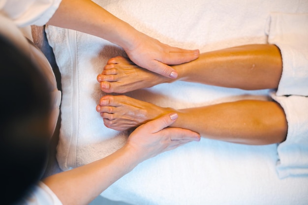 Foto bovenaanzicht van masseuses handen geven etherische olie massage aan de benen van een vrouw in de spa salon close-up poort...
