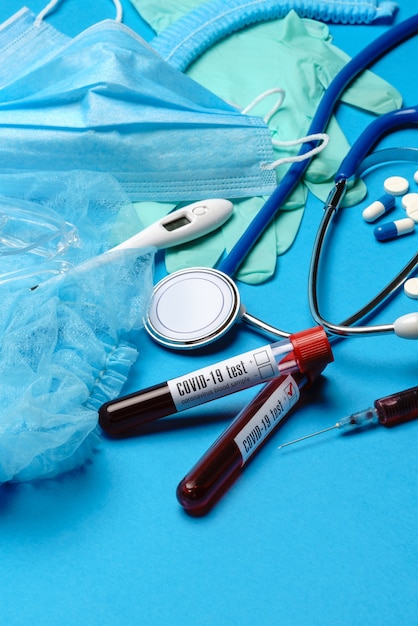 Foto bovenaanzicht van medische apparatuur en hulpmiddelen op blauwe ondergrond - stethoscoop, chirurgisch masker, medische handschoenen, spuit en bloed reageerbuis - gezondheidszorg en geneeskunde concept.