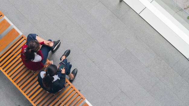 bovenaanzicht van meisjes groep gebruiken slimme telefoon en praten op houten bankje