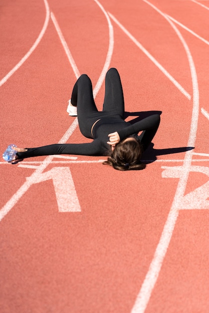 Bovenaanzicht van moe fit vrouw in sportkleding rusten na de training of hardlopen op een loopband rubberen stadion