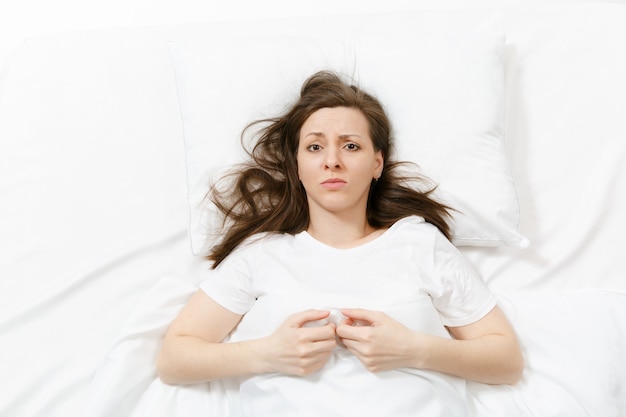 Bovenaanzicht van moe gestrest huilende jonge vrouw liggend in bed met wit laken, kussen, deken. Nadenkend gefrustreerd verdrietig overstuur vrouw tijd doorbrengen in de kamer