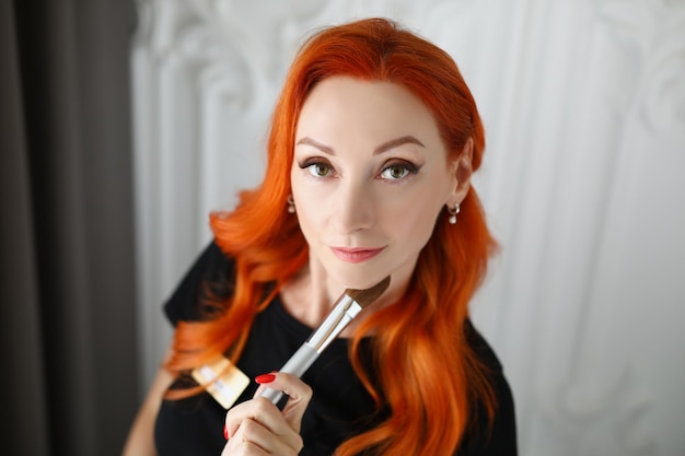 Bovenaanzicht van mooie roodharige make-up artiest poseren in schoonheidssalon met professional