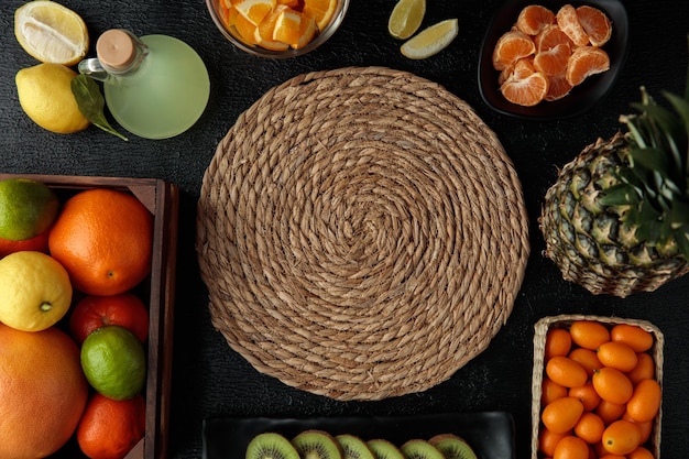 Foto bovenaanzicht van onderzetter voor warme gerechten met limoensap fruit als sinaasappel limoen mandarijn kumquats ananas kiwi sinaasappel en mandarijn plakjes op zwarte achtergrond