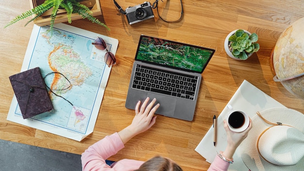 Foto bovenaanzicht van onherkenbare jonge vrouw met laptop en kaarten die vakantiereis vakantie plannen