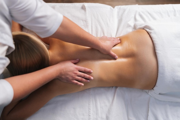Bovenaanzicht van onherkenbare mannelijke masseur masseren rug en schouder van jonge vrouw liggend op massagetafel in spa salon