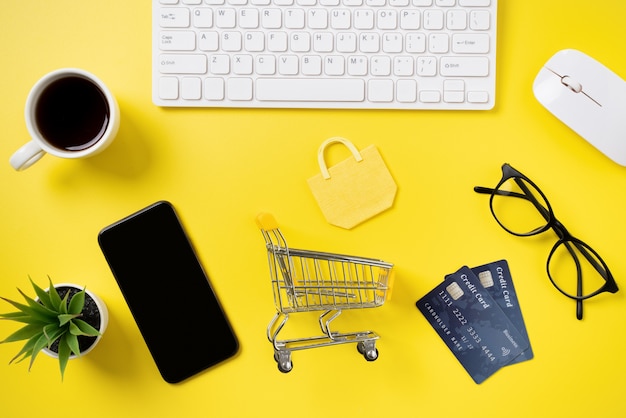 Bovenaanzicht van online winkelen concept met creditcard, slimme telefoon en computer geïsoleerd op kantoor gele tafel achtergrond.