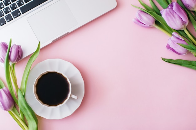 Bovenaanzicht van paarse tulpen met laptop en koffiekopje geïsoleerd op roze background