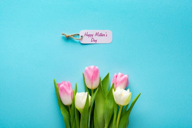 Bovenaanzicht van papieren label met happy mothers day belettering en tulpen op blauwe achtergrond