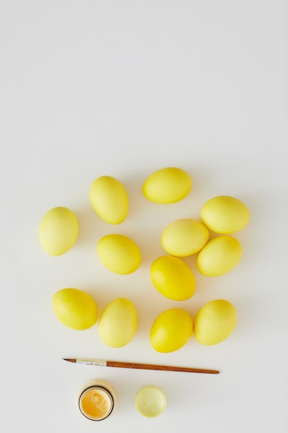Bovenaanzicht van pastel gele paaseieren met kwast aangeklaagd in minimale samenstelling op witte achtergrond, kopieer ruimte