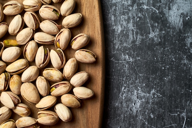 Bovenaanzicht van pistachenoten op een houten bord op een donkere achtergrond