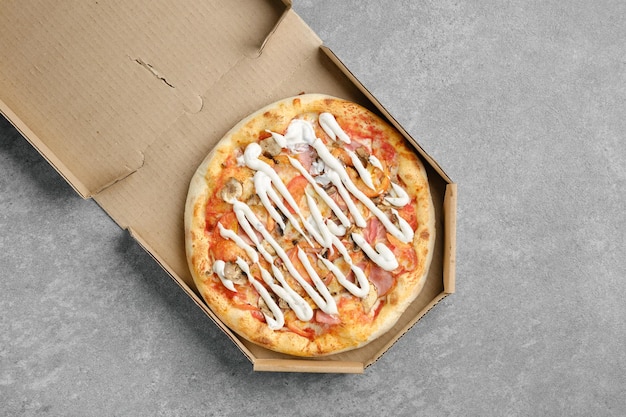 Bovenaanzicht van pizza met hamchampignon en plakjes tomaat bedekt met mayonaise in kartonnen doos