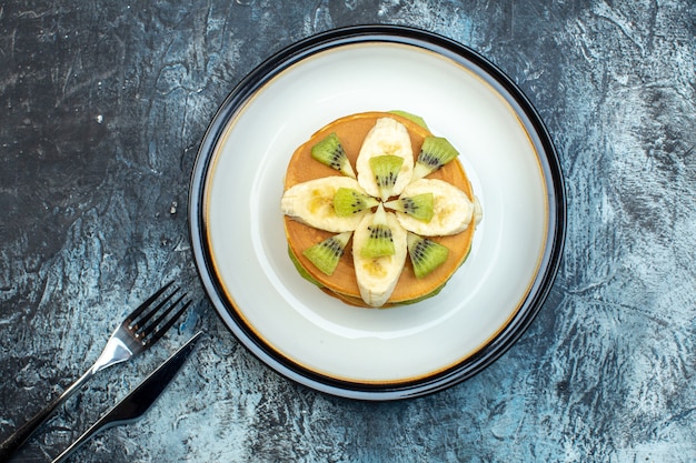 Bovenaanzicht van pluizige pannenkoeken in amerikaanse stijl gemaakt met natuurlijke yoghurt en gestapeld met lagen fruit op bord en bestek op ijsachtergrond met vrije ruimte