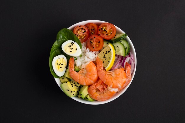 Bovenaanzicht van poke bowl met garnalen, rijst en groente op de zwarte achtergrond. Detailopname.