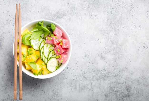 Bovenaanzicht van poke bowl met verse rauwe tonijn, fruit, groenten, ruimte voor tekst. Traditionele Hawaiiaanse schotel op rustieke stenen achtergrond. Gezond en schoon eten concept. Poke met plakjes vis, kopieer ruimte