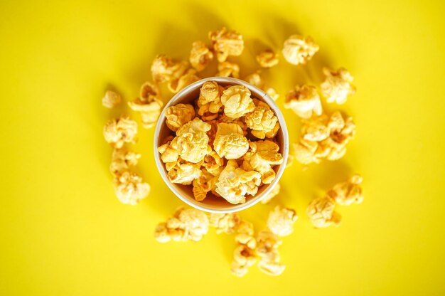 Bovenaanzicht van popcorn in papieren glas op geel papier achtergrond