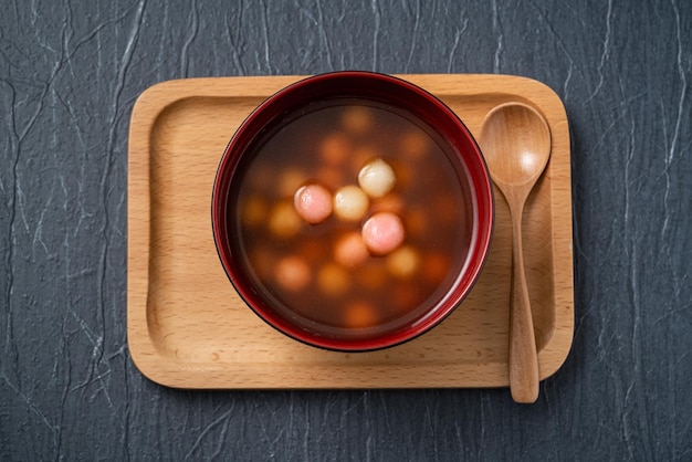 Bovenaanzicht van rode en witte tangyuan (tang yuan, kleverige rijst knoedelballen) met zoete siroopsoep in een kom op blauwe tafelachtergrond voor winterzonnewende festivalvoedsel.