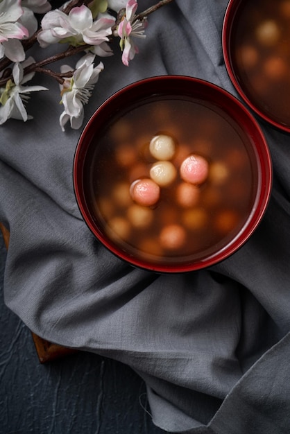 Bovenaanzicht van rode en witte tangyuan (tang yuan, kleverige rijst knoedelballen) met zoete siroopsoep in een kom op blauwe tafelachtergrond voor winterzonnewende festivalvoedsel.