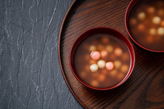 Bovenaanzicht van rode en witte tangyuan (tang yuan, kleverige rijst knoedelballen) met zoete siroopsoep in een kom op blauwe tafelachtergrond voor winterzonnewende festivalvoedsel.