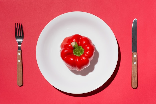 Bovenaanzicht van rode paprika op witte plaat met mes en vork op rode achtergrond