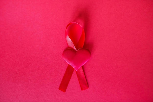 Bovenaanzicht van rood lint en klein rood hart, symbool voor kankerbewustzijn, op geïsoleerde pastelrode achtergrond