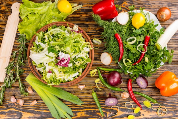 Bovenaanzicht van rozemarijn, sla, prei, ui, paprika, citroen en andere heerlijke ingrediënten op houten tafel