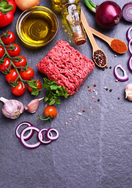 Bovenaanzicht van rundvlees gehakt met kruiden en groenten en meer voedsel op zwarte ondergrond